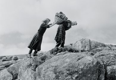 Women carrying basket up rocks