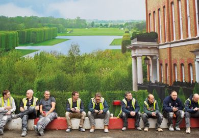 Workmen sit in front of hoarding depicting English country house and grounds Workmen sit in front of hoarding depicting English country house and grounds