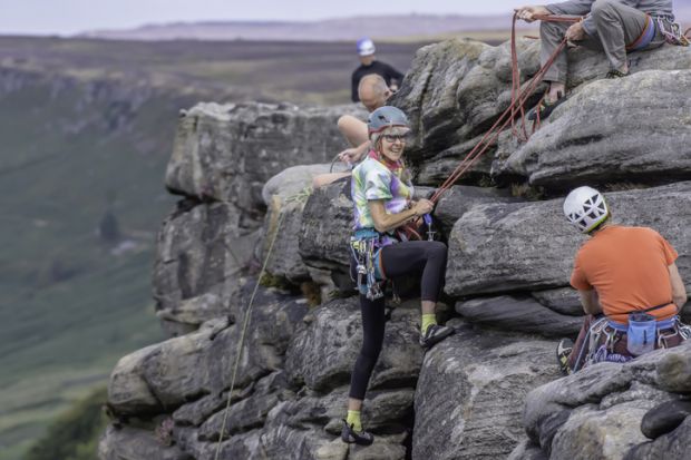 08.01.2018.Stanage Edge,Derbyshire,Uk.Active seniors.Mature woman-rock climber finishing climbing route with smile on her face.Group of climbers on cliff edge.Blurred landscape in background.