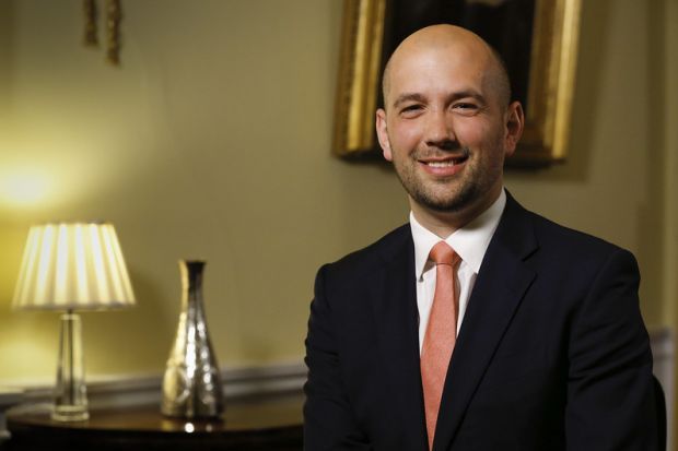 Ben Macpherson, a bald man wearing a suit, smiles at the camera