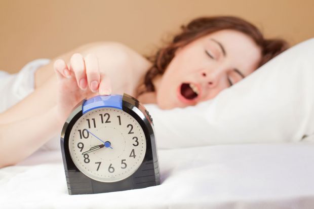 Yawning woman pressing alarm snooze button