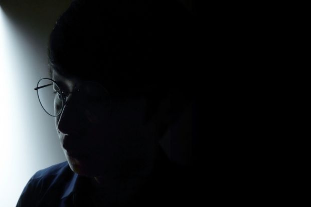 Asian man wearing glasses and thinking in dark