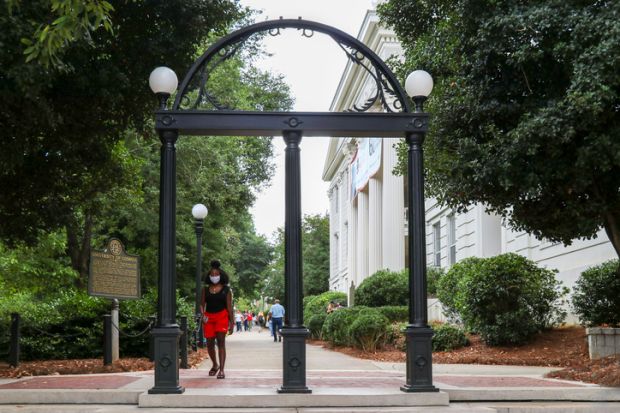 Athens, Georgia - August 27, 2021 A student wearing a protective face mask walks through the Arch at the entrance to the University of Georgia's historic North Campus.