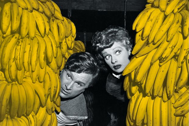 Man and woman peer out from behind bunches of bananas
