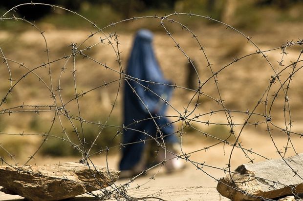 A covered Muslim woman walks behind some barbed wire