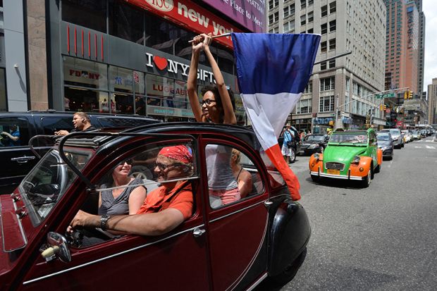 A woman holds a French flag as she rides in a parade of Citroen cars from the Greater New York Citroën and Velosolex Touring Club on Bastille Day in New York, USA. To illustrate a surge in interest in European jobs from US researchers.