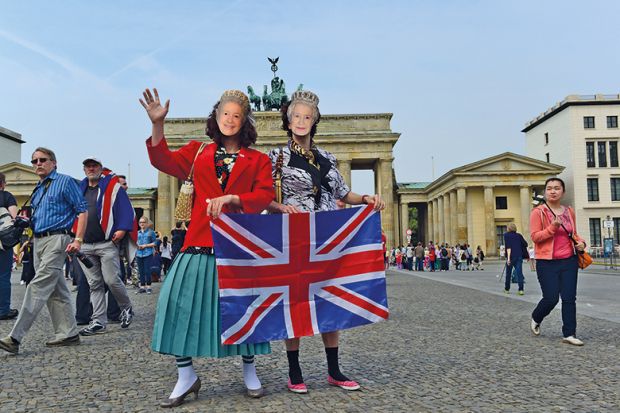 Pair wearing queen masks and holding Union Jack in front of Brandenburg Gate