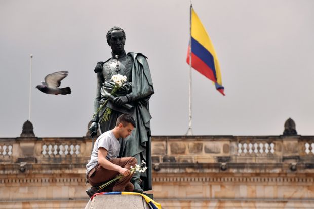 A colombian youngster places the national flag and a bunch of white flowers at the bottom of Simon Bolivar's monument in Bogota. A colombian youngster places the national flag and a bunch of white flowers at the bottom of Simon Bolivar's monument in Bogota.