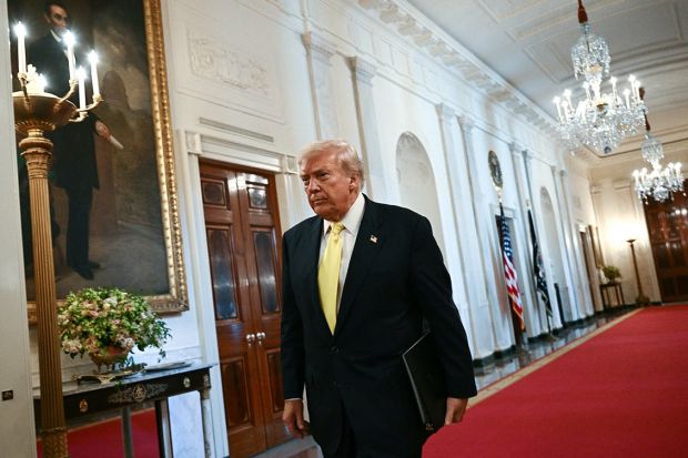 US President Donald Trump walks down a hallway in the White House.
