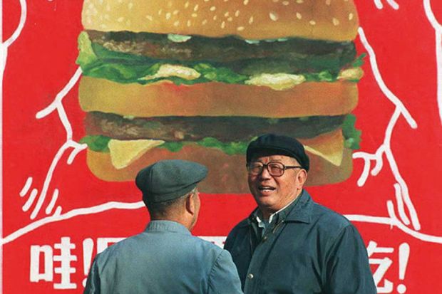 Two Chinese men in front of a billboard advertisement for a burger