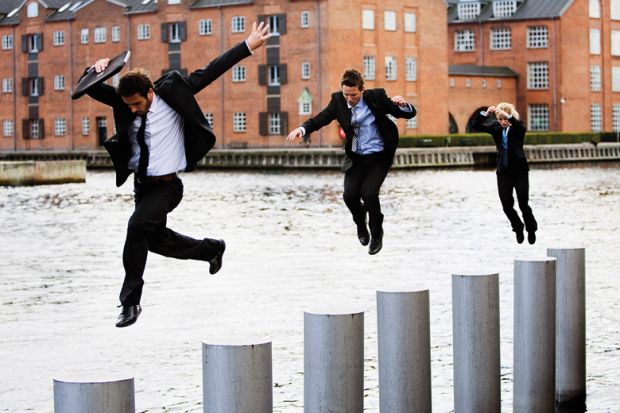 Businesspeople jumping across pillars in city river