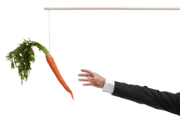 Businessperson's hand reaching for carrot on stick