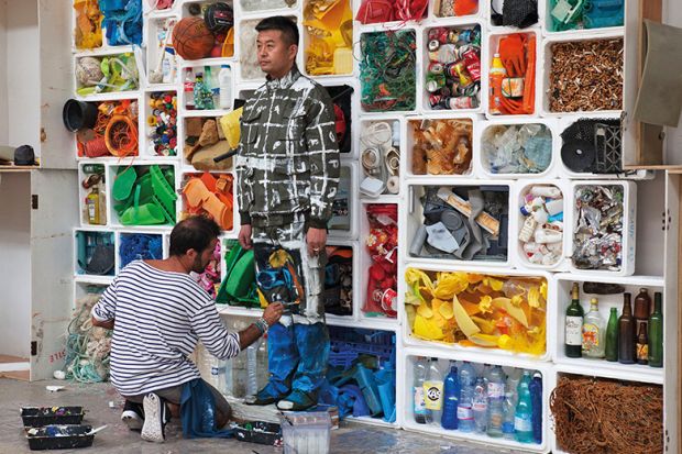 Camouflage artist Liu Bolin at the Surfrider Foundation in Biarritz, blended into a background of rubbish, 2017