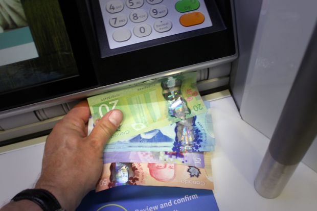 Someone takes Canadian money from an ATM
