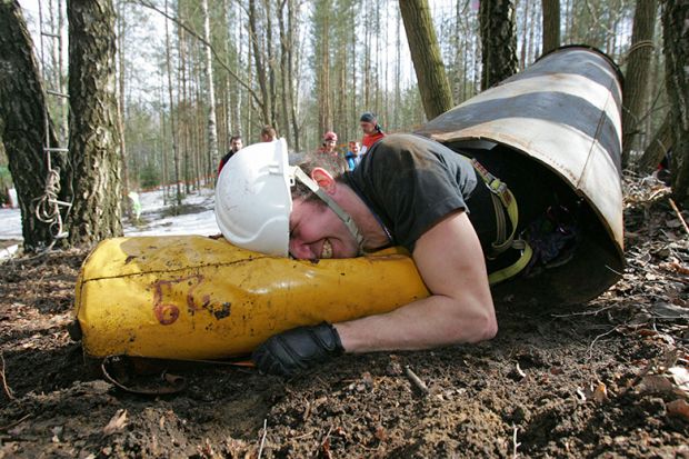 A speleologist crawls with his caving pack through a tunnel during a competition. To illustrate staff feeling forced to publish in a 'narrow' subset of elite journals to boost REF standing.