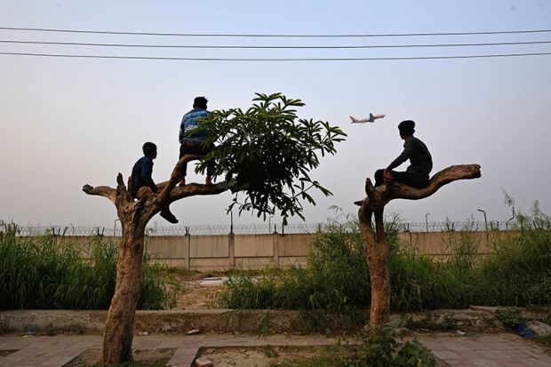 People climb trees to watch the take off of an airplane along a highway, outside Indira Gandhi International Airport in New Delhi, India. To illustrate that setting up a branch campus in India may be costly, limited in reach and difficult to scale.
