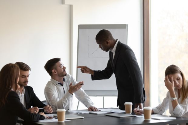 People gesticulate at each other in a business meeting, symbolising conflict within business schools