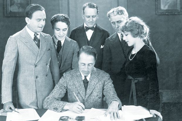 Filmmaker D. W. Griffith reviews the contract of Mary Pickford, accompanied by (l-r) her husband, Douglas Fairbanks, and Charlie Chaplin, and their two attorneys. Illustrating jump in teaching contracts under REF