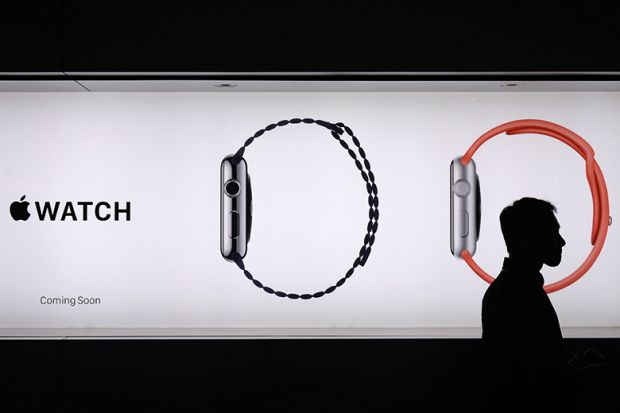 A man walks past a billboard ad for Apple watches, his head encircled by one of the images