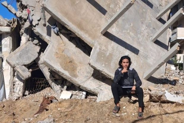 A young student in Gaza sitting near the ruins of his home