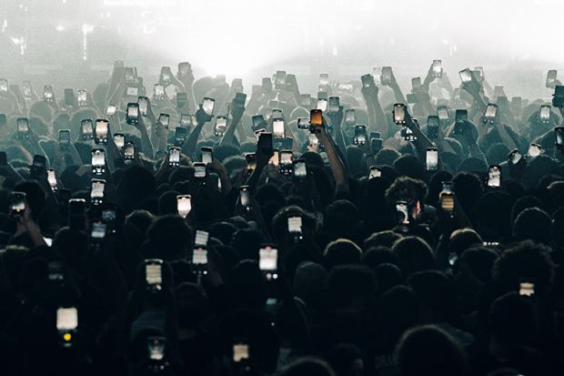 A crowd holding up mobile phones. To illustrate ‘near universal’ AI use leading to ‘polarisation’ among students.