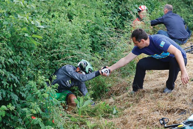 Two men helping cyclists who fell off their bikes