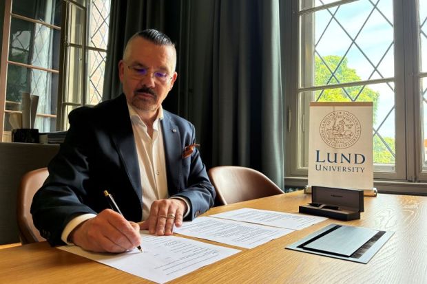 Lund vice-chancellor Erik Renstrom sitting at a desk, signing a document, with a sign that says Lund University on the desk