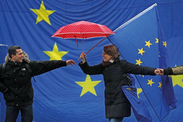 A man reaches for another participant in front of a giant European flag during a pro-European Union rally