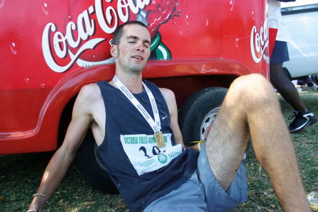 Exhausted marathon runner sitting by Coca-Cola branded vehicle