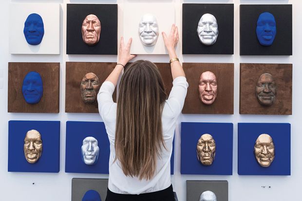 A woman with her back to the camera places a number of differently coloured face masks on a wall