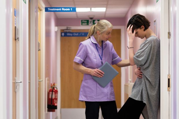 Female nurse comforts young woman in hospital corridor