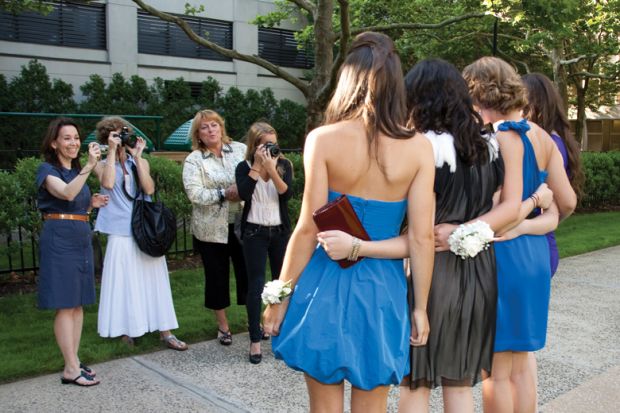 Female students being photographed by their mothers and sister before senior prom