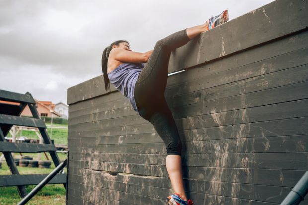 Female participant in an obstacle course climbing a wall illustrating gender inequality in economics