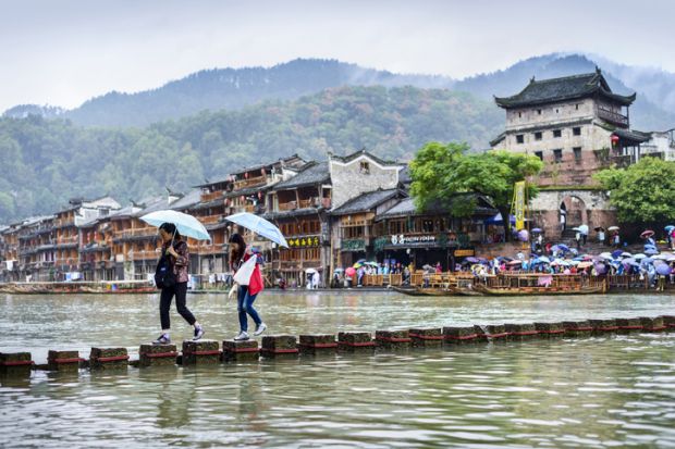 Fenghuang, China - September 19, 2015 The Old Town of Phoenix (Fenghuang Ancient Town). people are getting across the Tuojiang River in a drizzling day