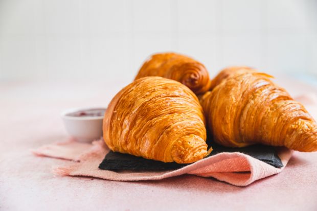Fresh crispy croissants with red berry jam on slate board, pink background
