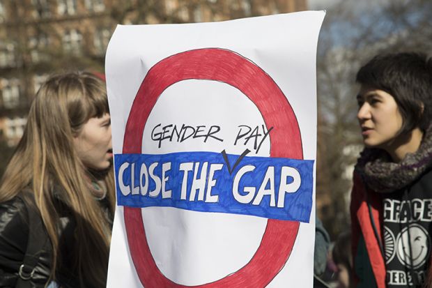 Women behind a sign stating 'close the gender pay gap' during International Women's Day in London, UK.