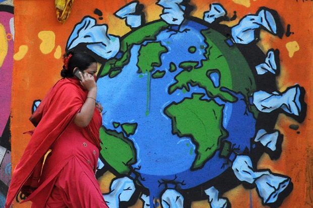 A woman on a phone walks past a graffiti depicting world map affected with Coronavirus. India.
