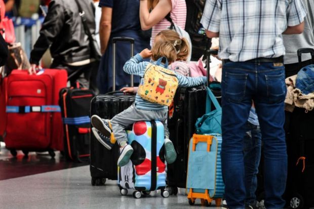 Travellers sit on their suitcases at the check-in counters