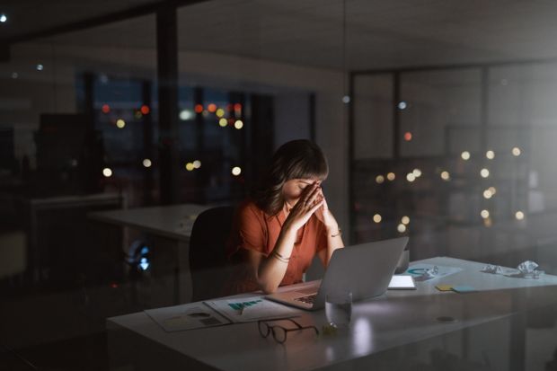 A woman looking stresed while working on a laptop in a dimly lit room