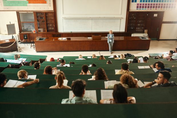 A wide lecture hall with students in tiered seating with green desks