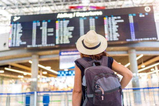 A woman wearing a straw hat and a backpack is standing in front of a large airport display