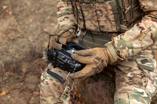 A soldier sitting down and remotely controlling a drone