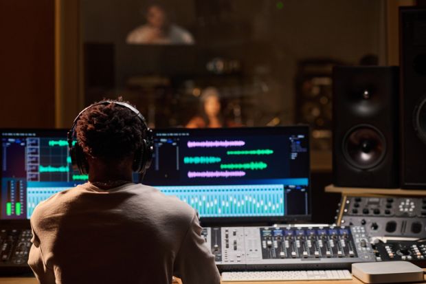 Young Adult Man Wearing Headphones Monitoring Audio Levels in Studio 
