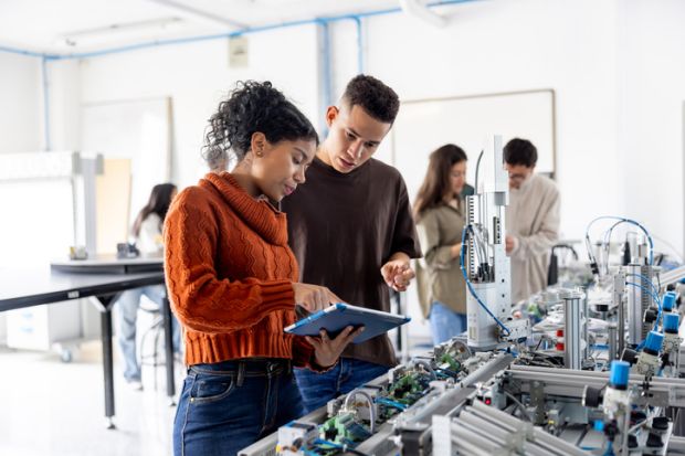 A male and female student using a digital tablet while operating a production line robot in a lab.