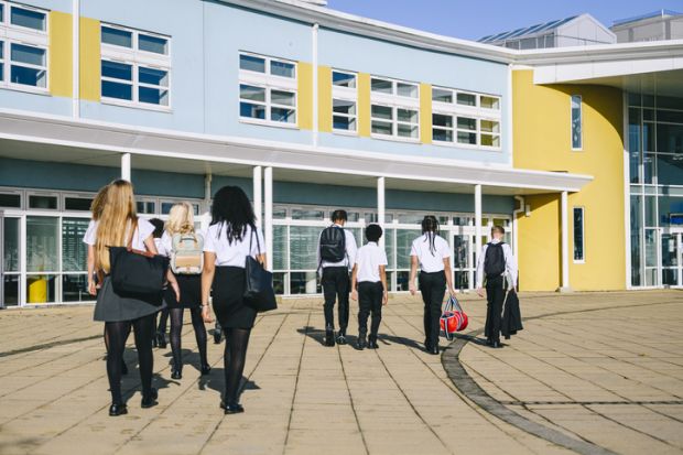 school students wearing uniform walking to school entrance carrying bags
