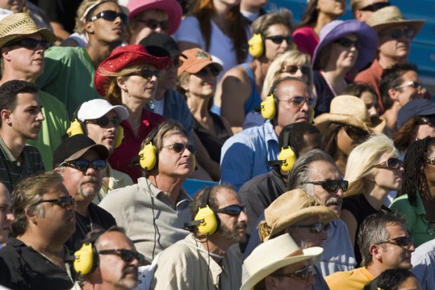 People in stadium watching car racing, listening to headphones People in stadium watching car racing, listening to headphones