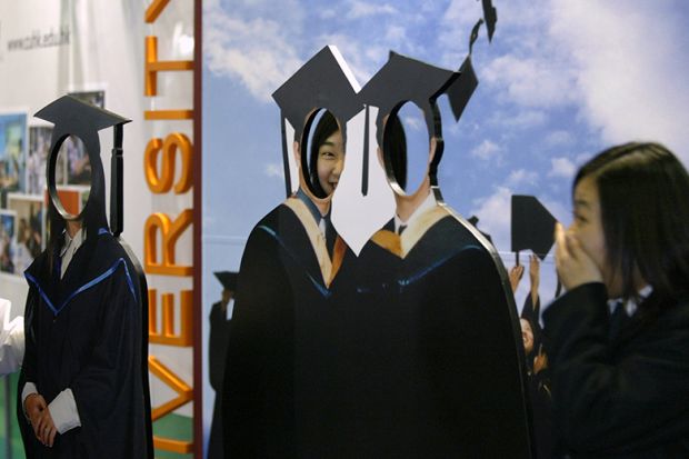 Visitors to a careers expo peek through a cardboard cut out of graduates. To illustrate 'fake' students which can be pushed by recruitment agents.