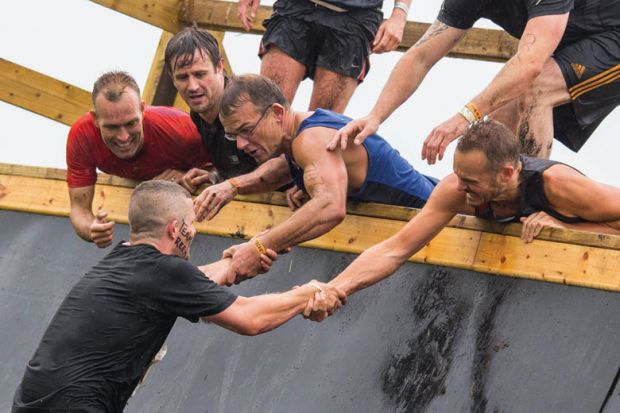 Group of men assisting teammate on obstacle course
