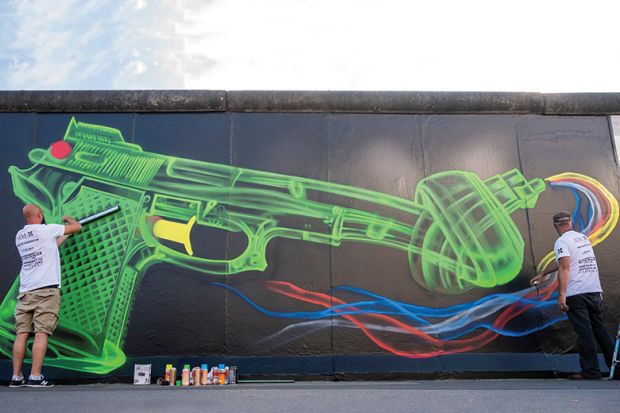 Street artists create an updated likeness of Swedish artist Carl Fredrik Reuterswaerd’s famous “Knotted Gun” sculpture on a segment of the former Berlin Wall, 2020