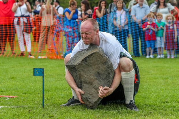 Man struggling to lift a stone at the Highland Games in Dundonald, Scotland. To illustrate a shortfall in funding for Scottish universities. Man struggling to lift a stone at the Highland Games in Dundonald, Scotland. To illustrate a shortfall in funding for Scottish universities.